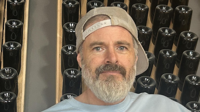 Un homme en portrait devant des bouteilles de vin.