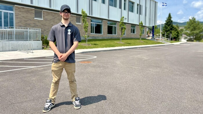 Un jeune garçon pose devant une école.