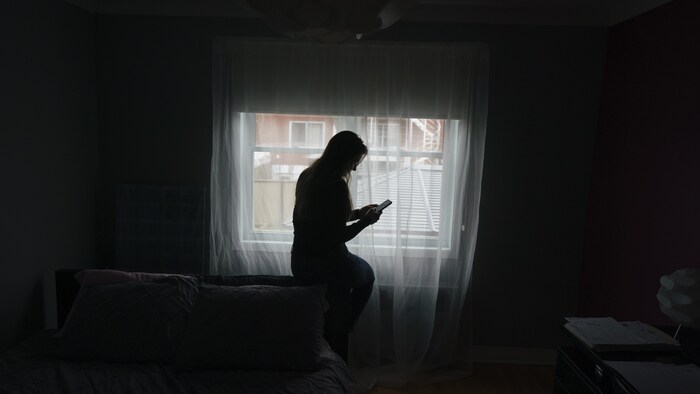 Une femme regarde son téléphone dans une chambre.