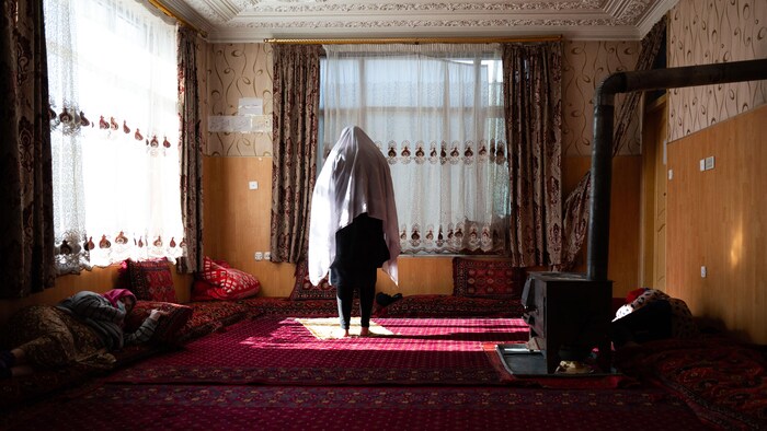 Une femme debout et deux autres couchées dans une pièce.