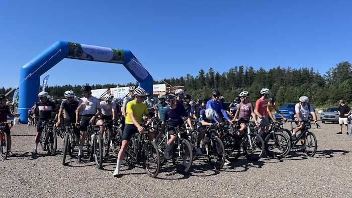 Un groupe de cyclistes équipés de casques est rassemblé sur un terrain de gravier au départ d'une course.