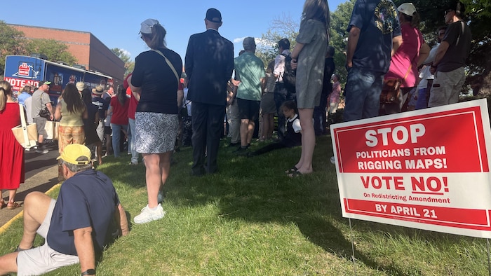 Des partisans du « non » écoutent un discours, le 16 avril 2025, devant le bureau de vote de Leesburg, en Virginie. Sur la pelouse, des militants ont planté une pancarte sur laquelle on peut lire « Empêchez les politiciens de truquer nos cartes! Votez non! ».