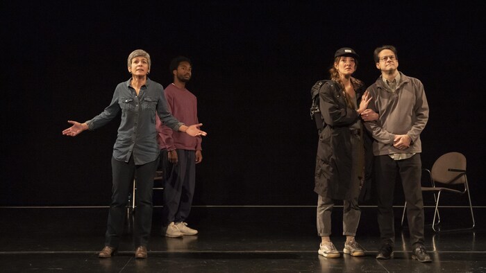 Sur la scène d'un théâtre, quatre interprètes, se tiennent face au public.