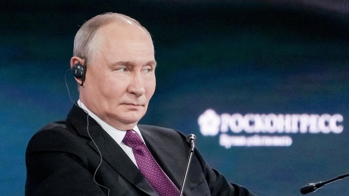 Vladimir Poutine, l'air sérieux, écoute avec une oreillette de traduction simultanée dans l'oreille.