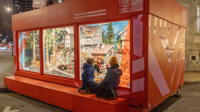 Des enfants regardent une vitrine de Noël. 