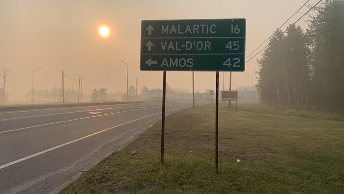 Un panneau routier aperçu dans un brouillard de fumée, avec le soleil à l'arrière.
