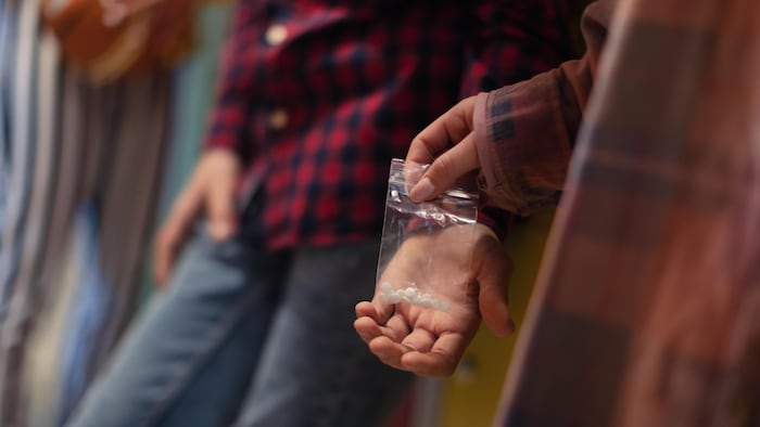 Une adolescente donne subtilement un sac rempli de pilules à un jeune dans ce qui semble être le couloir d'une école secondaire.