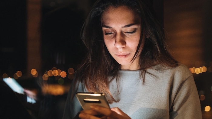 Une femme regarde l'écran de son téléphone cellulaire.