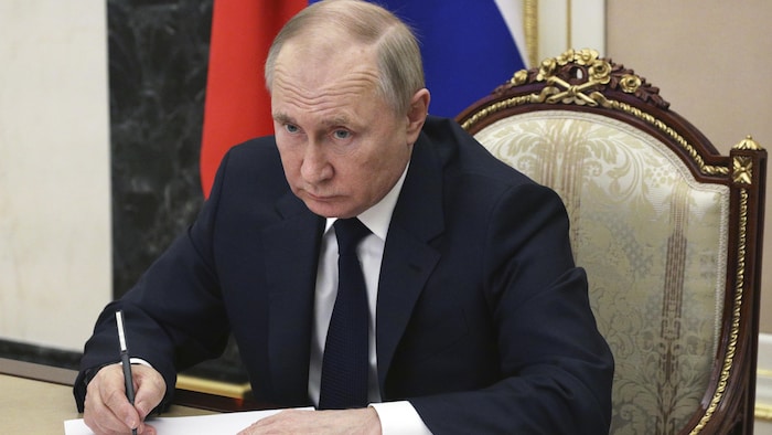 الرئيس الروسي فلاديمير بوتين جالساً إلى طاولة وبيده قلم يكتب به على ورقة بيضاء.