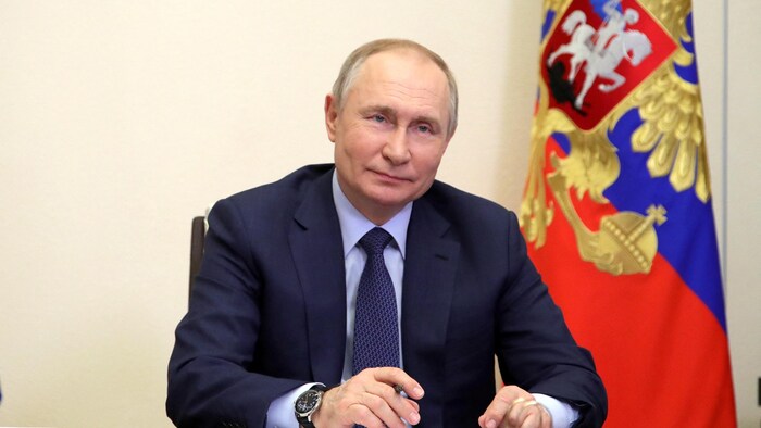 فلاديمير بوتين جالس إلى طاولة وخلفه علم روسيا.