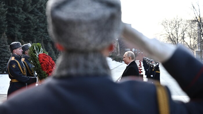 Vladimir Poutine se tient debout devant une couronne de fleurs, sous le regard de plusieurs soldats.