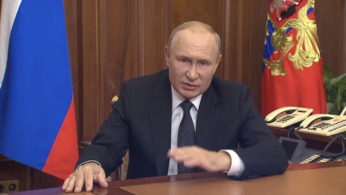 Assis derrière son bureau présidentiel, Vladimir Poutine prononce un discours.
