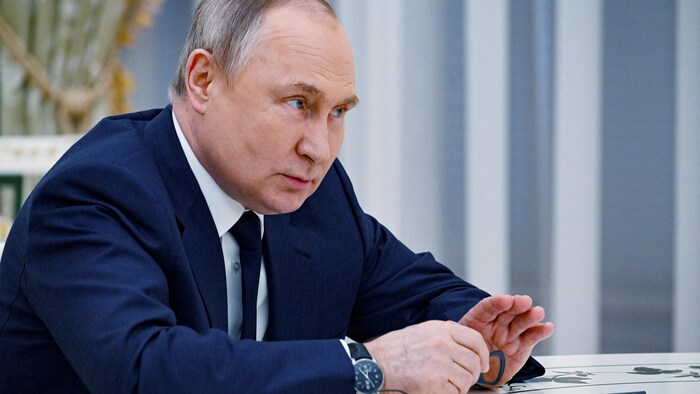 Vladimir Poutine, assis à table, discute.