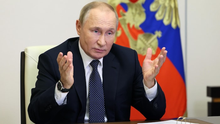 الرئيس الروسي فلاديمير بوتين جالساً إلى طاولة ورافعاً ذراعيه أمامه.