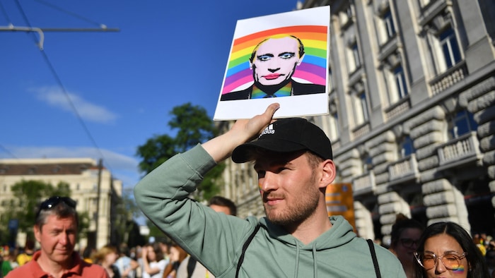 Une personne tient un portrait arc-en-ciel de Vladimir Poutine.