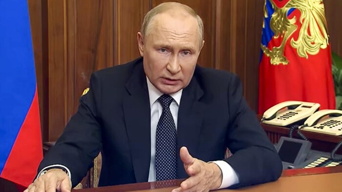 Le président Vladimir Poutine parle à la télévision, dans une salle montrant des drapeaux.
