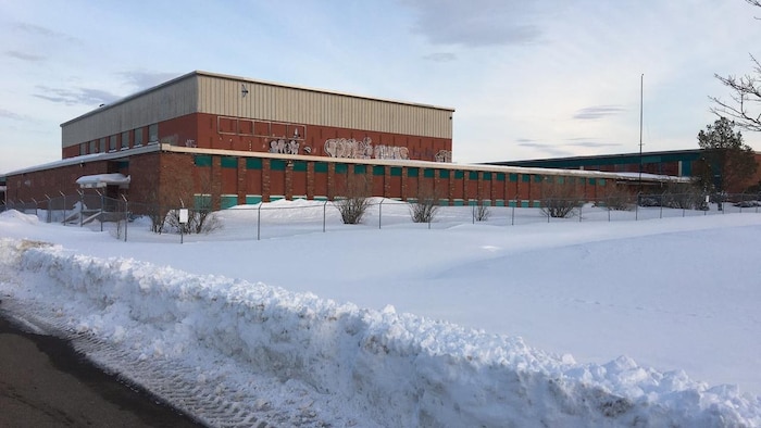 Un vieux bâtiment austère, brun et beige, décoré de graffiti, sur un terrain enneigé.