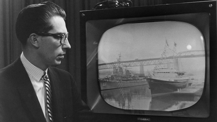 Dans un studio de télévision, Bruce Marsh, debout, regarde un moniteur de télévision dans lequel on voit le yacht royal
Britannia faire son entrée dans la Voie maritime.