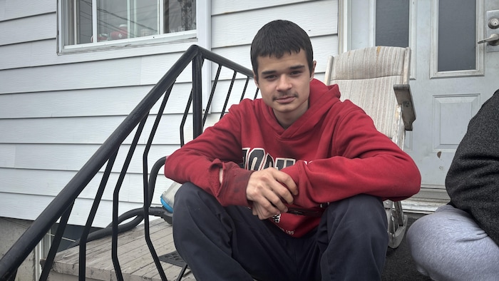 Un jeune homme assis sur les marches de son balcon. 
