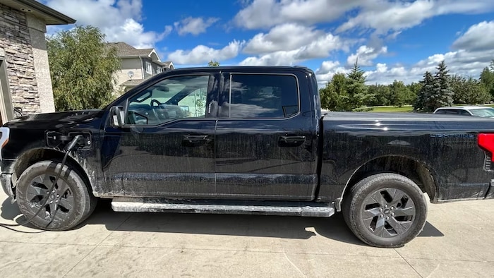 Une Ford F-150 Lightning Lariat 2023 en plan centrale devant un garage, une journée ensoleillée. 