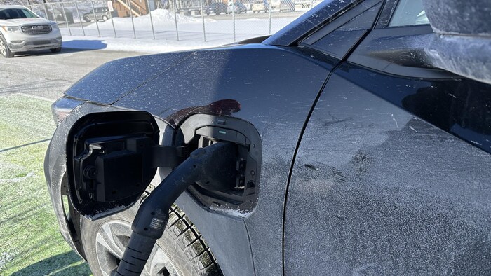 Le devant d'une voiture branchée à une borne de recharge.
