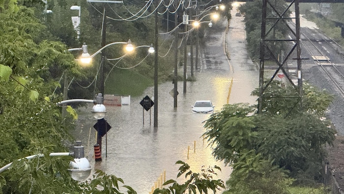 Une voiture submergée dans une rue inondée en bordure d’une autoroute. 