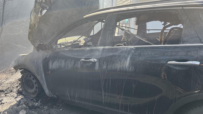 Une voiture brûlée à côté d'une maison dont seulement le revêtement a été endommagé.