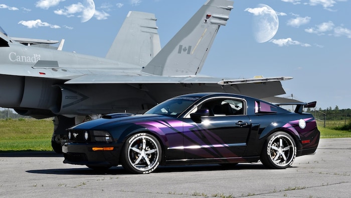 Une voiture Mustang près d'un avion de combat. 