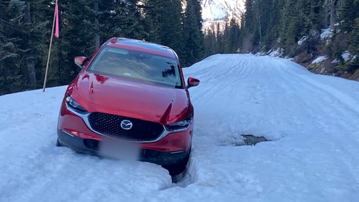 Une voiture rouge coincée dans une vingtaine de centimètres de neige sur un chemin forestier pas déneigé.