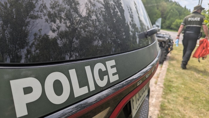 Un policier marche avec deux bouteilles d'eau dans une main et des vestes de flottaison dans l'autre.