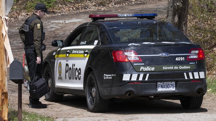 Une voiture et un agent de la Sûreté du Québec dans un secteur boisé.