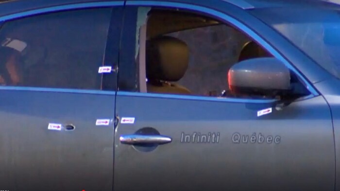 Une voiture de couleur grise sur laquelle sont affichés des autocollants indiquant les impacts de projectiles d’armes à feu.