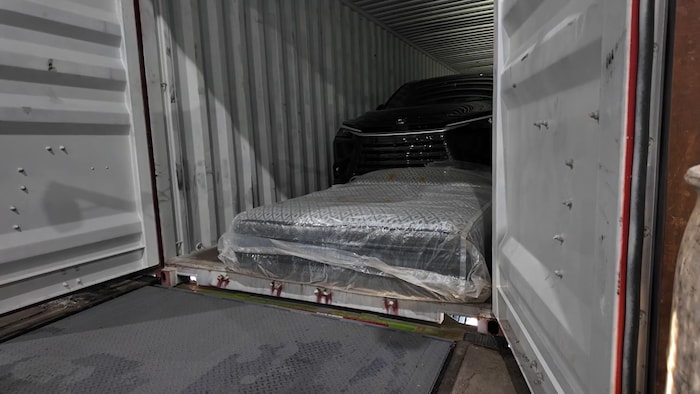 Une voiture dans le fond d'un conteneur et partiellement cachée par des matelas posés au sol.