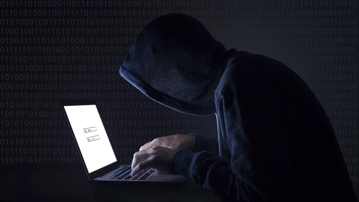 Un homme portant un chandail avec capuchon est penché sur un ordinateur.