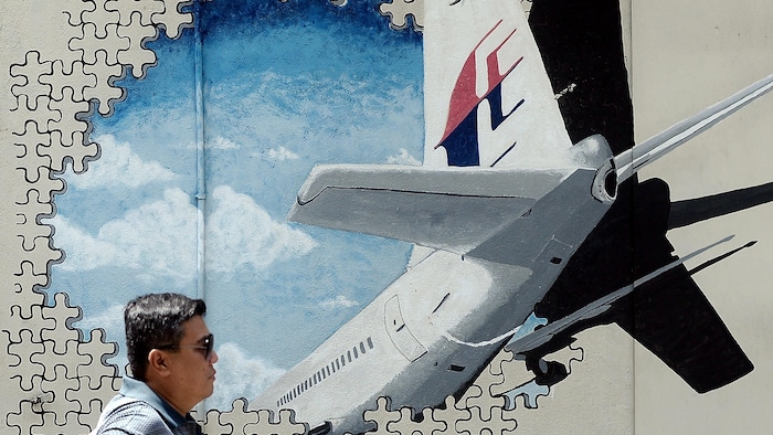 Un homme portant des lunettes de soleil marche devant une murale représentant la queue de l'avion de Malaysia Airlines qui a disparu au-dessus de l'océan Indien.
