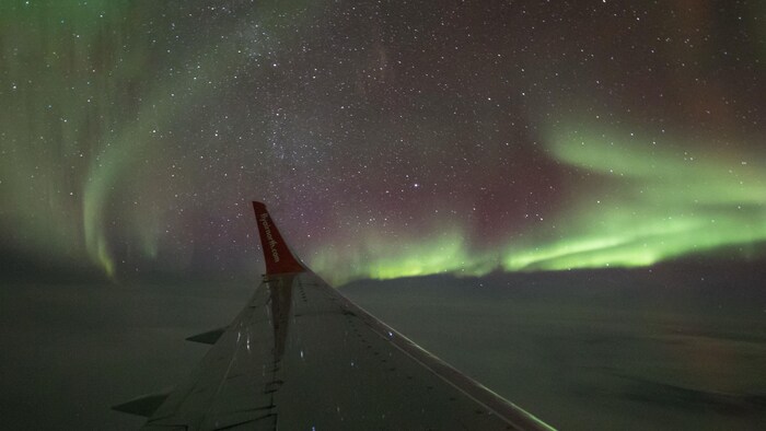 Des aurores boréales dans le ciel, vues par le hublot d'un avion