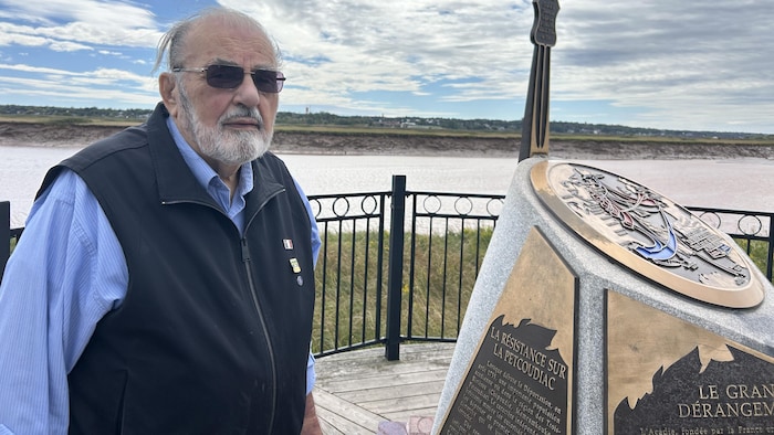 Jean J. Gaudet pose devant le monument sur le bord de la rivière.