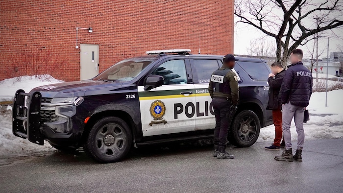 Des policiers de la SQ surveillent une personne en état d'arrestation à côté d'une autopatrouille.