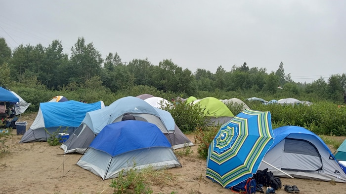 Des tentes se dressent au milieu d'un terrain de sable et de buissons.