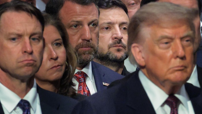 Dans une foule, derrière le président Donald Trump, on aperçoit le visage de Volodymyr Zelensky.