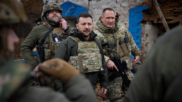 Volodymyr Zelensky porte un habit militaire et est entouré de soldats. 
