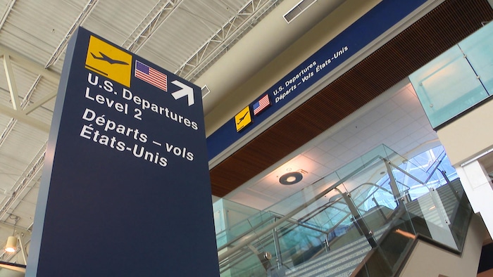 L'enseigne dans l'aéroport qui pointe vers un escalier roulant determination    se rendre à l'endroit determination    les départs des vols vers les États-Unis.