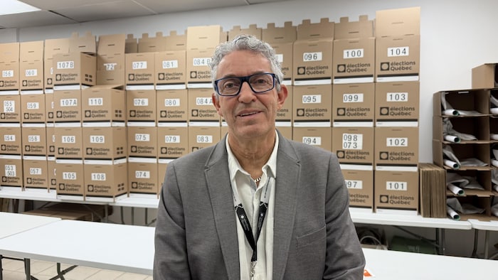 Gilbert Grenon devant des boîtes de scrutin empilées.