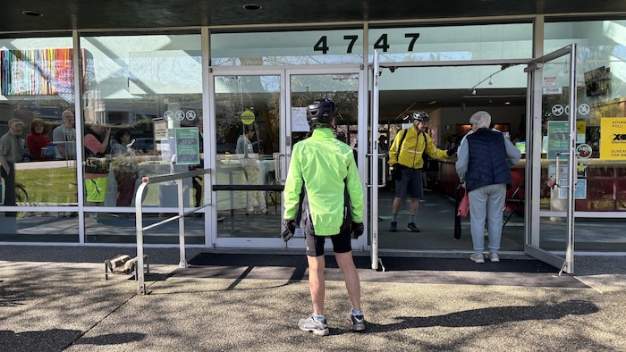 Un homme habillé pour faire du vélo regarde vers l'intérieur d'un bureau de vote où des électeurs attendent.