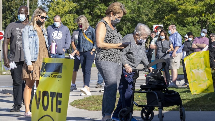 Des gens de tous âges attendent en file. Une affiche indique « Vote ».