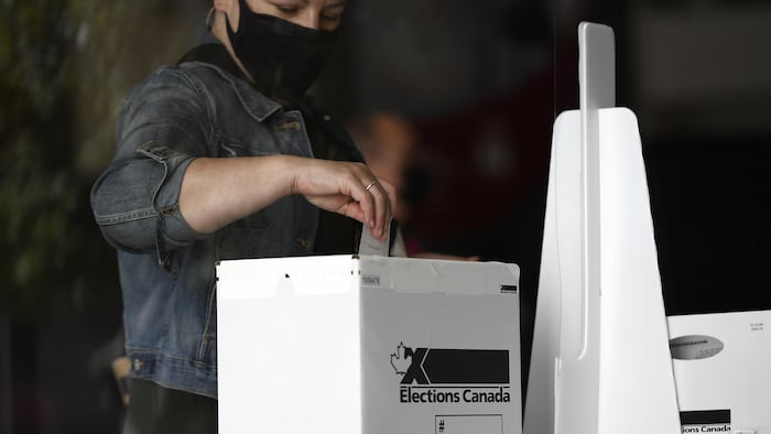 شخص يرتدي قناع وجه واقياً يسقط ورقة الاقتراع في الصندوق.