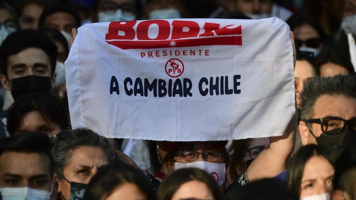 Une personne tient un fanion sur lequel il est écrit  : Boric président, changeons le Chili.