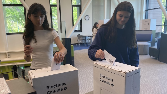 Deux jeunes élèves mettent des bulletins de vote dans les urnes.