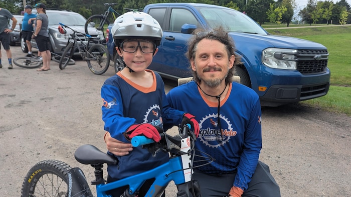 Un père s'agenouille auprès de son petit garçon, qui tient son vélo de montagne.