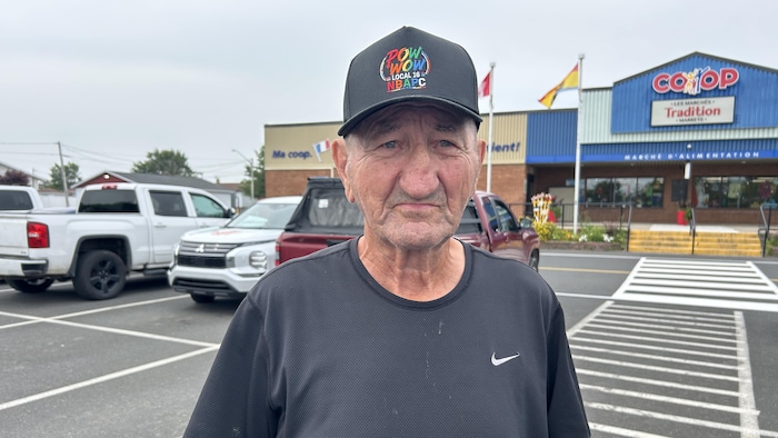 Un homme avec une casquette décorée du mot «Pow Wow» en lettres multicolores affiche un air sérieux.